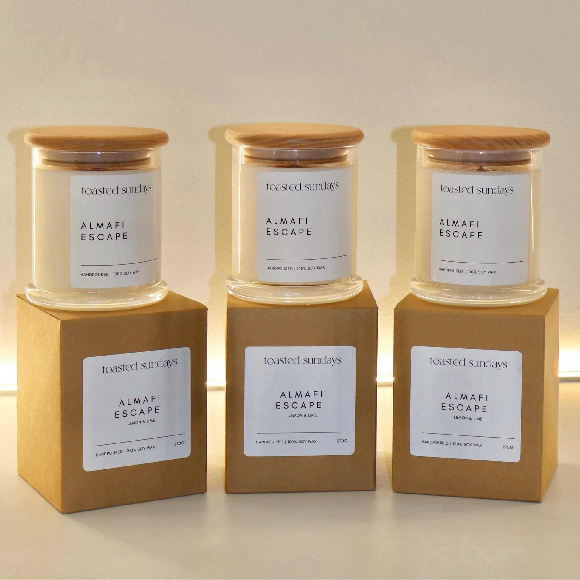 Three candles labeled 'Almari Escape' on wooden stands with a neutral background