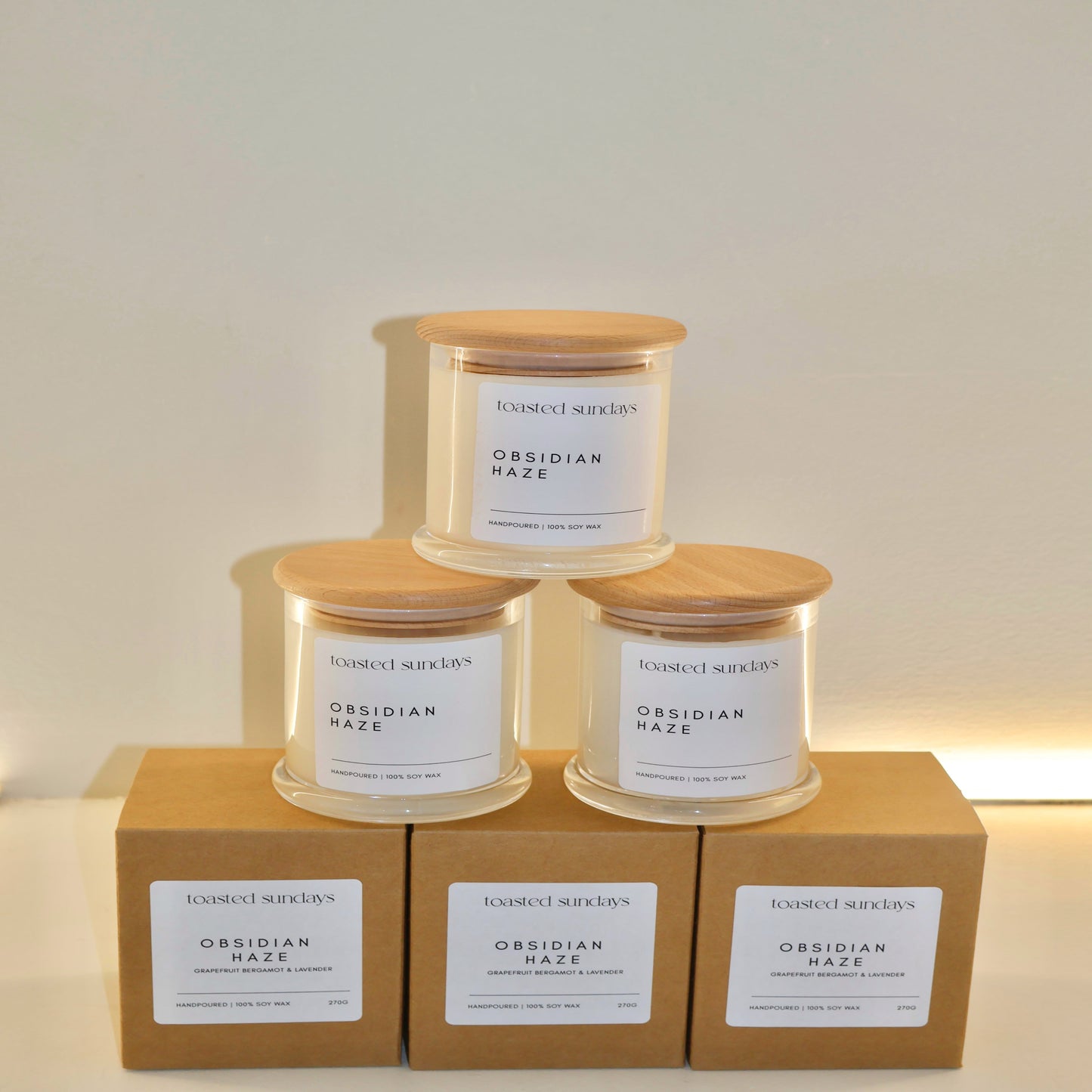 Three candles with wooden lids on top of cardboard boxes against a white background