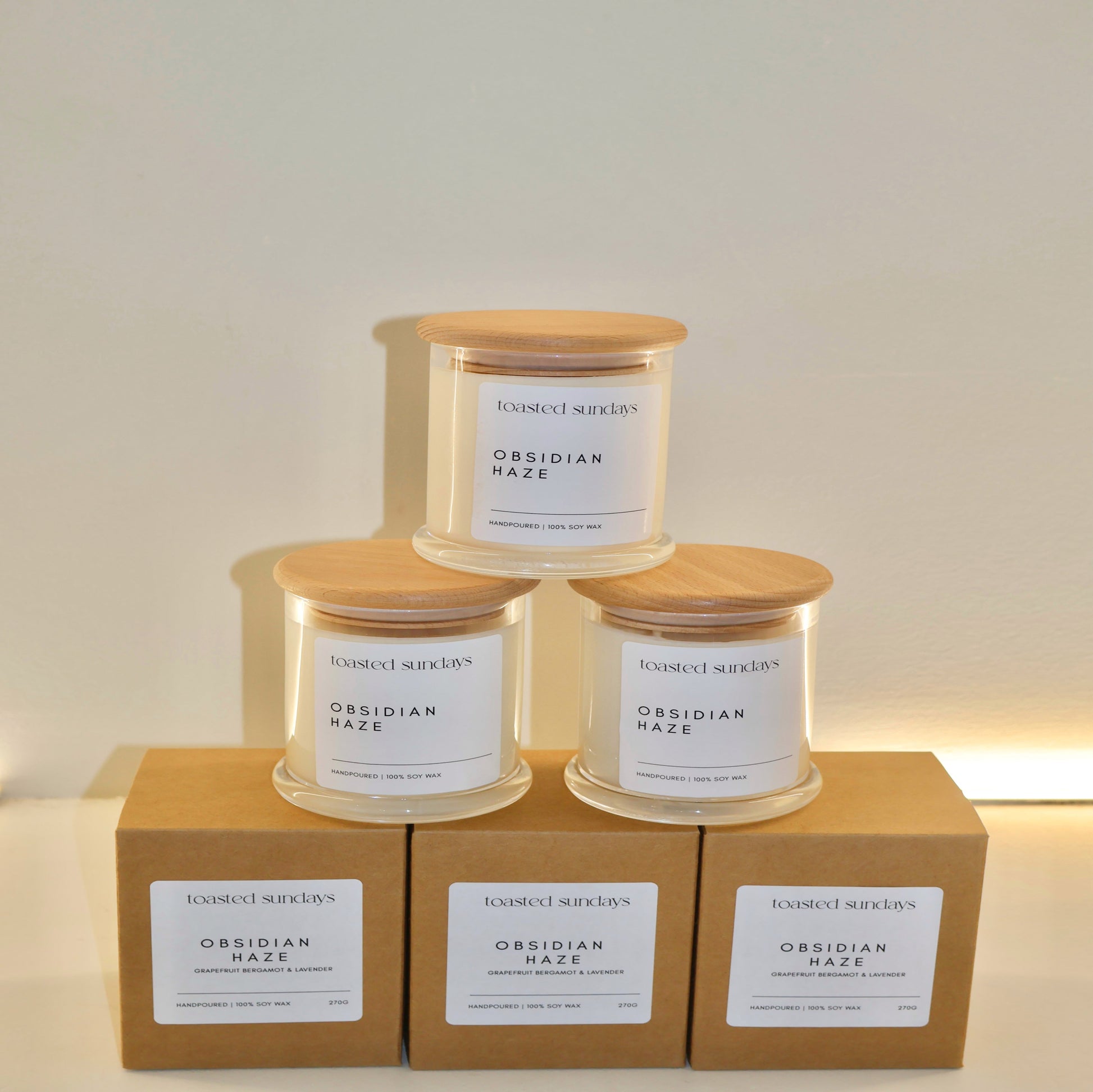 Three candles with wooden lids on top of cardboard boxes against a white background