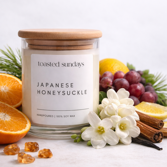 Candle labeled 'Toasted Sundays Japanese Honeysuckle' with fruits and flowers on a white background