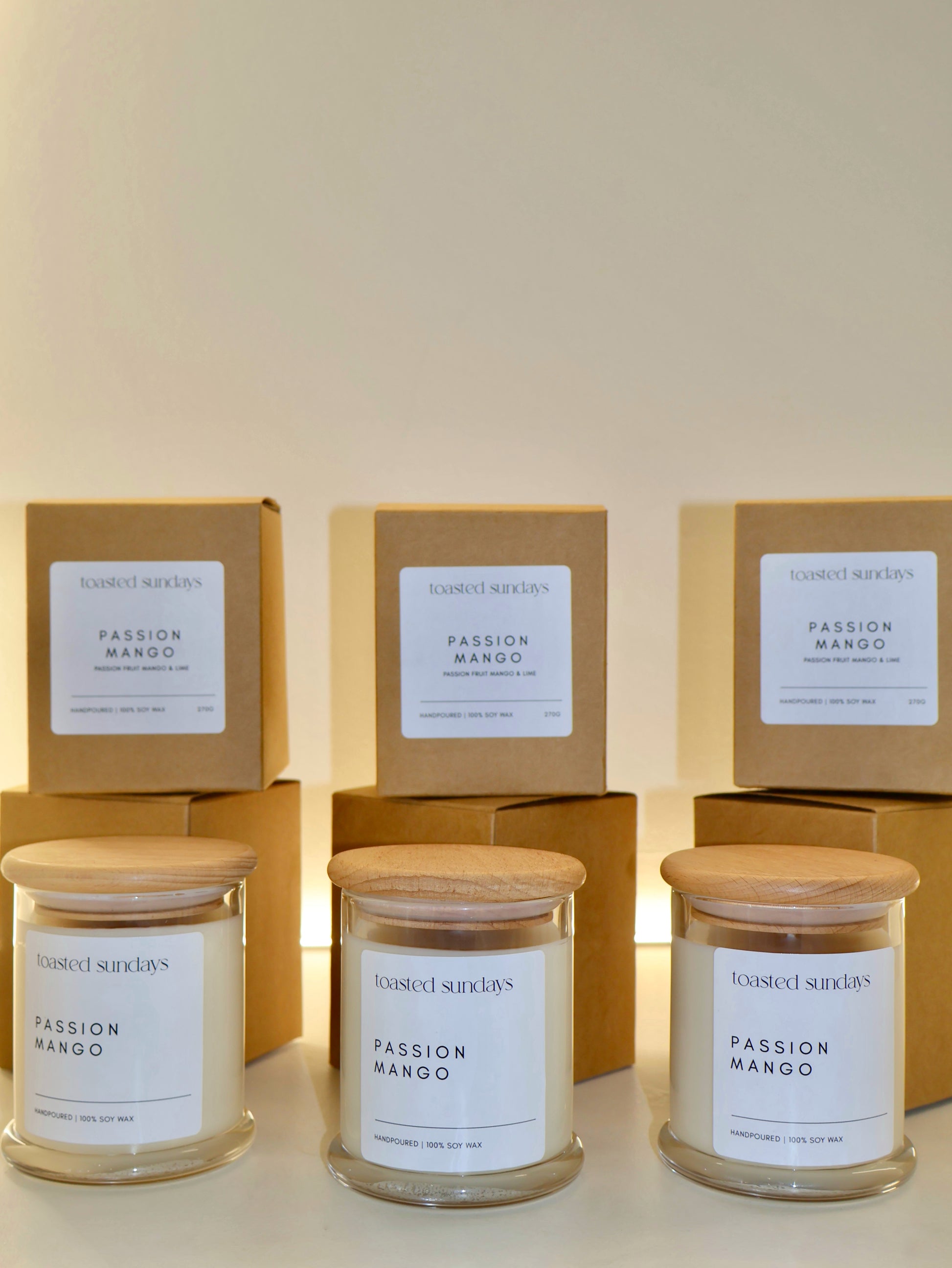 Three 'Passion Mango' candles with their packaging on a light background